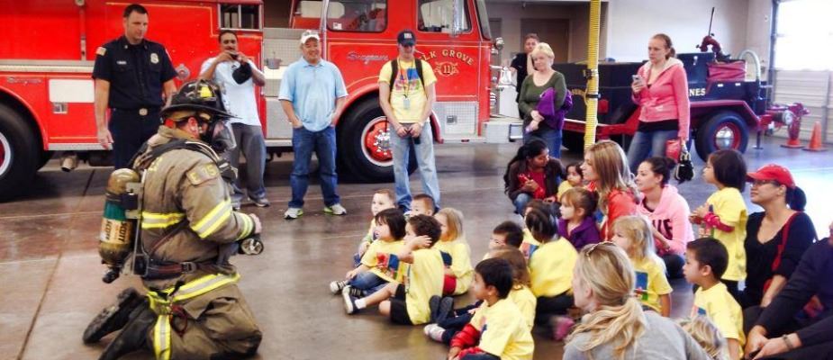 Children sit on the floor and listen as a fire fighter in full gear gives a demonstration