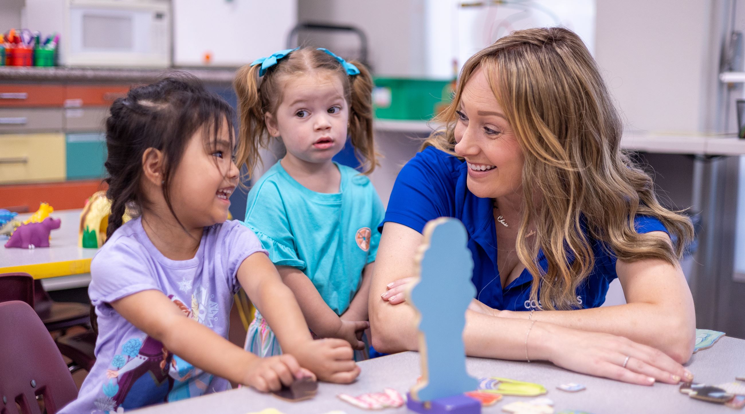 A teacher smiles at a group of toddlers.